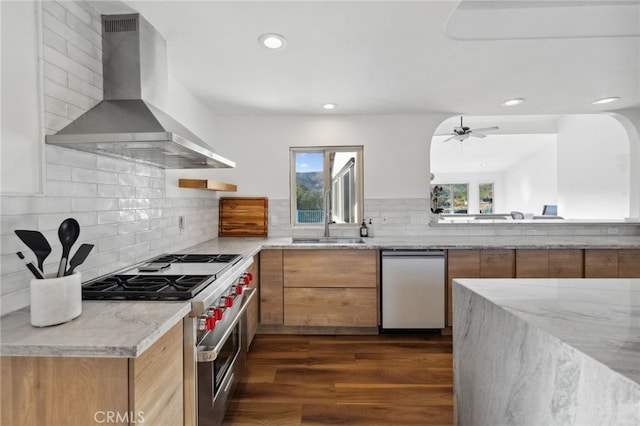 kitchen with sink, light stone counters, appliances with stainless steel finishes, dark hardwood / wood-style flooring, and wall chimney range hood