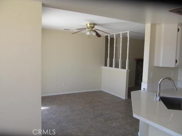 interior space with baseboards, white cabinets, ceiling fan, light countertops, and a sink