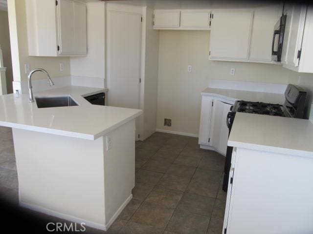 kitchen with a peninsula, a sink, white cabinetry, light countertops, and stainless steel gas stove