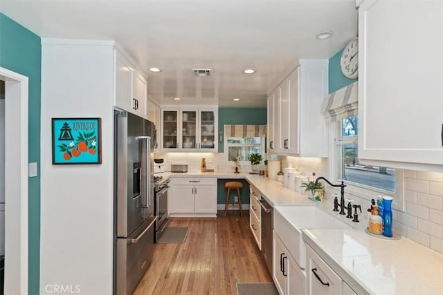 kitchen with light stone counters, premium appliances, light hardwood / wood-style floors, white cabinets, and decorative backsplash