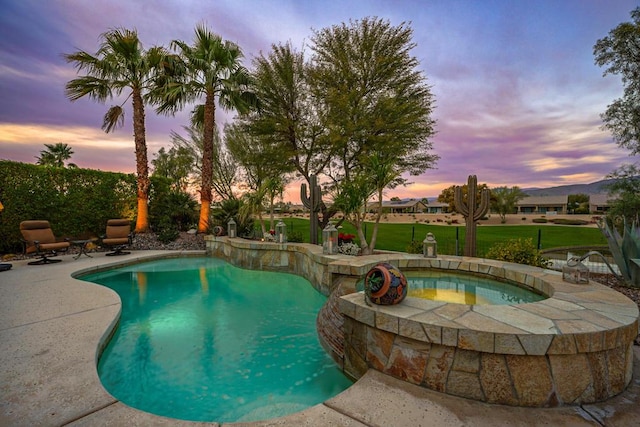 pool at dusk featuring an in ground hot tub, a yard, and a patio area