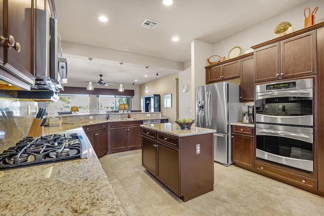 kitchen featuring appliances with stainless steel finishes, a center island, light stone countertops, decorative light fixtures, and kitchen peninsula