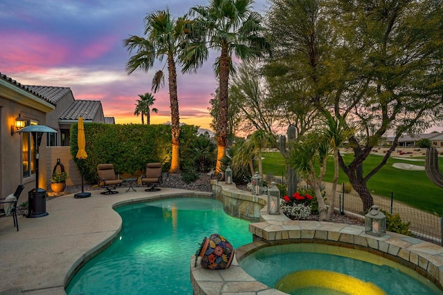 pool at dusk with an in ground hot tub and a patio