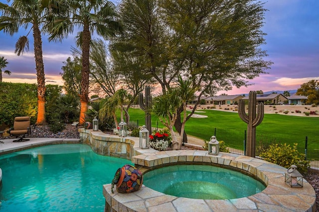 pool at dusk with an in ground hot tub and a yard