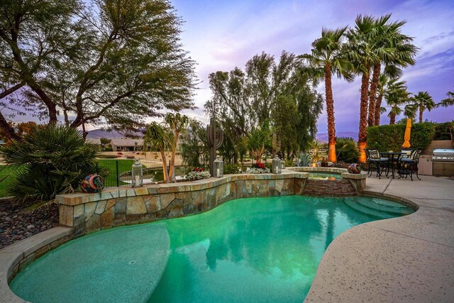 pool at dusk featuring grilling area, a patio, and an in ground hot tub