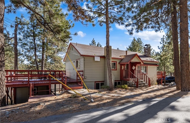 view of front of property with roof with shingles, a chimney, and a wooden deck