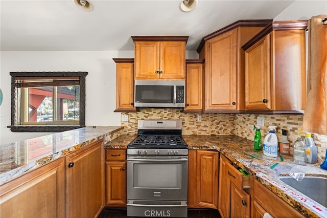 kitchen featuring stainless steel appliances, brown cabinets, backsplash, and dark stone countertops