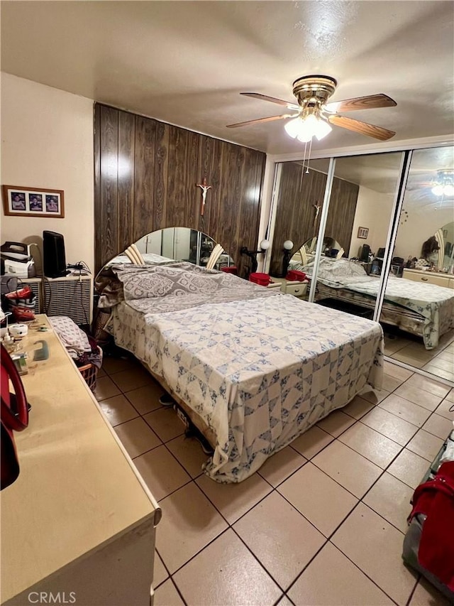 bedroom featuring ceiling fan, wooden walls, and light tile patterned floors