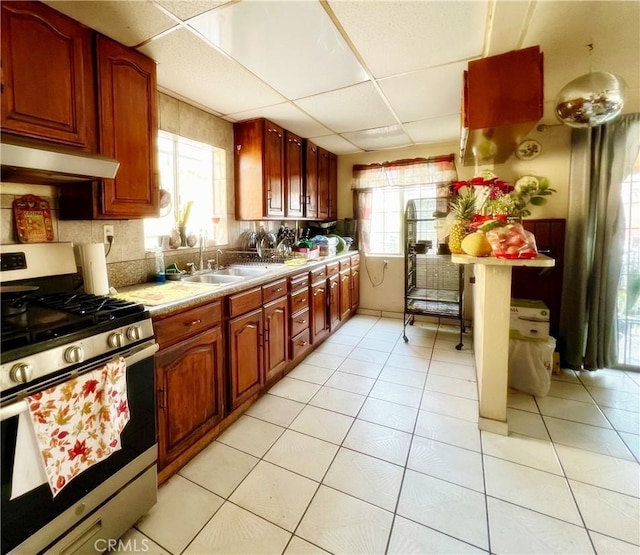 kitchen featuring a drop ceiling, sink, stainless steel gas range oven, and light tile patterned flooring