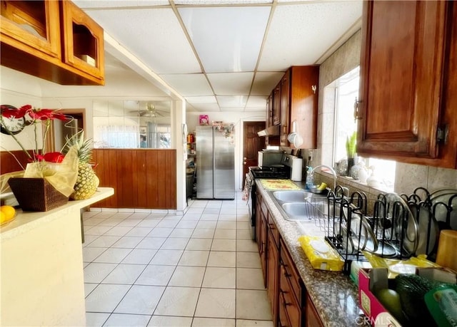 kitchen featuring sink, a paneled ceiling, light tile patterned floors, stainless steel refrigerator, and stove