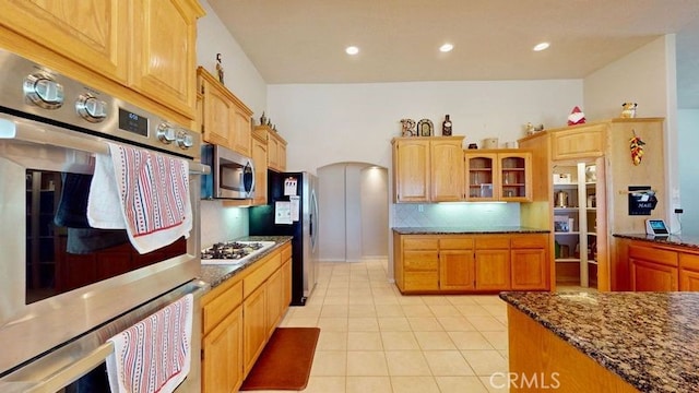 kitchen with appliances with stainless steel finishes, dark stone countertops, light tile patterned floors, and decorative backsplash