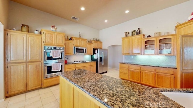 kitchen featuring backsplash, light tile patterned floors, stainless steel appliances, and dark stone counters