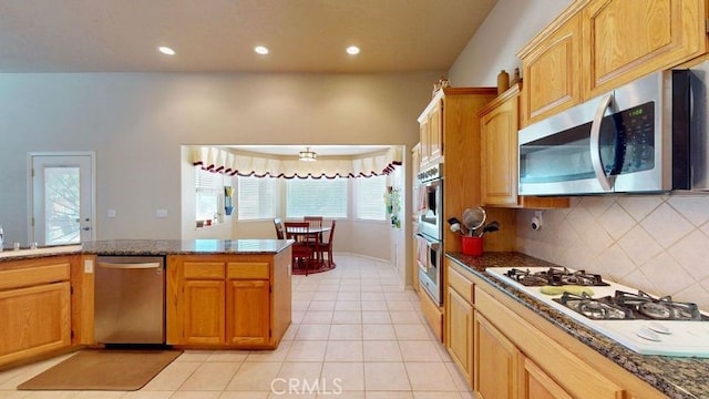 kitchen featuring light tile patterned floors, dark stone countertops, stainless steel appliances, tasteful backsplash, and kitchen peninsula