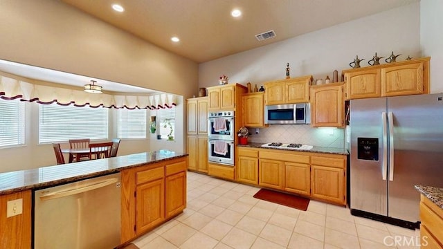 kitchen with light tile patterned floors, decorative backsplash, stainless steel appliances, and dark stone counters