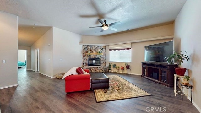 living room with ceiling fan, a stone fireplace, dark hardwood / wood-style flooring, and a textured ceiling