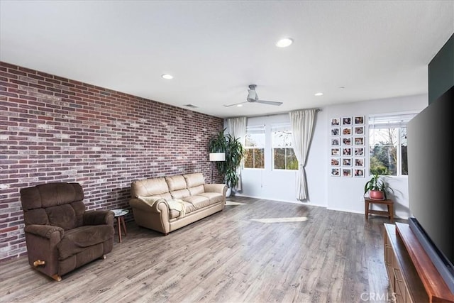 unfurnished living room with ceiling fan, brick wall, and light wood-type flooring