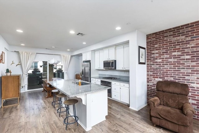 kitchen with appliances with stainless steel finishes, sink, white cabinets, a kitchen bar, and a center island with sink