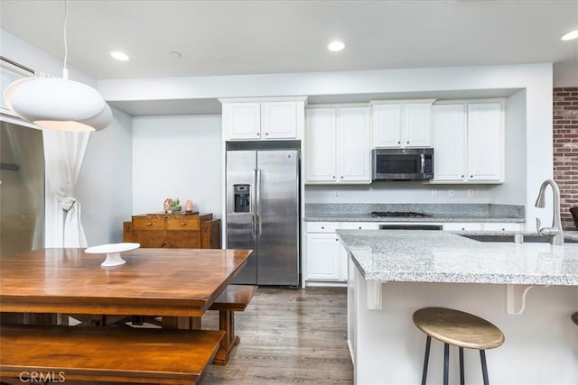 kitchen featuring stainless steel appliances, white cabinetry, light stone counters, and decorative light fixtures