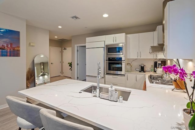 kitchen featuring a kitchen breakfast bar, built in appliances, light stone counters, white cabinets, and kitchen peninsula