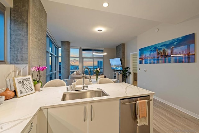 kitchen with stainless steel dishwasher, light stone countertops, sink, and light hardwood / wood-style flooring