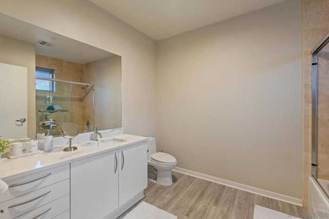 full bathroom with wood-type flooring, toilet, vanity, and bath / shower combo with glass door