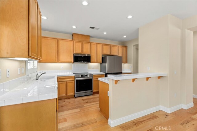 kitchen featuring light brown cabinetry, sink, a kitchen breakfast bar, stainless steel appliances, and light hardwood / wood-style flooring