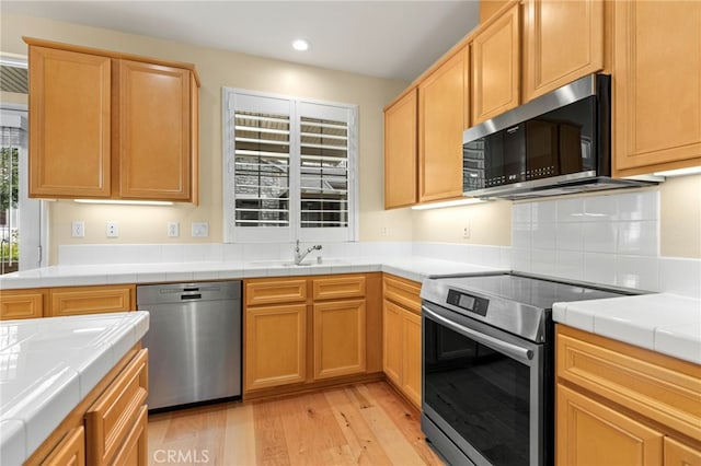 kitchen featuring appliances with stainless steel finishes, sink, tile counters, and light hardwood / wood-style flooring