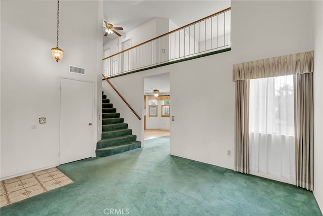 unfurnished living room featuring a towering ceiling, ceiling fan, and carpet