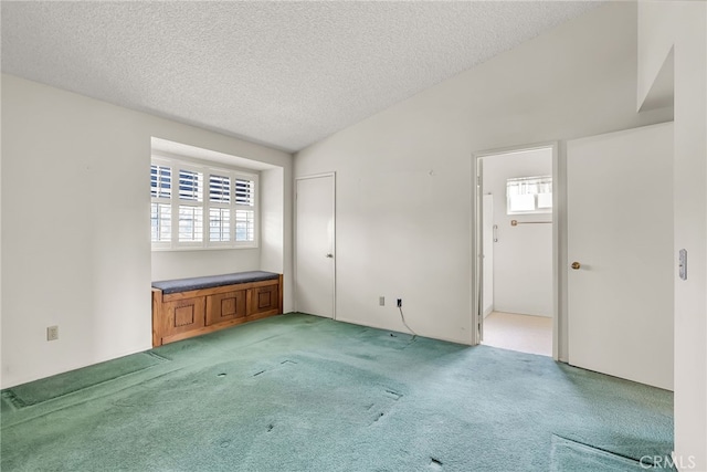 spare room featuring light colored carpet, vaulted ceiling, and a textured ceiling