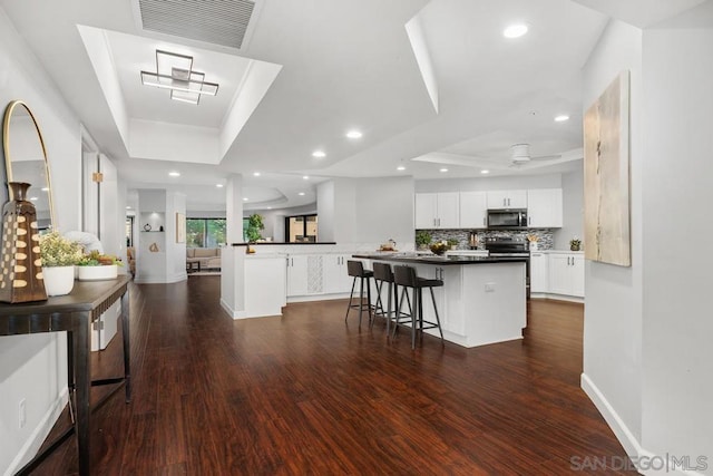 kitchen with appliances with stainless steel finishes, white cabinetry, a kitchen bar, kitchen peninsula, and a raised ceiling