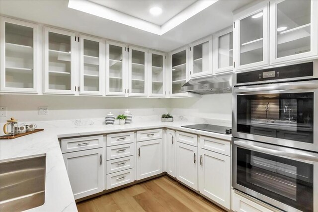 kitchen with black electric cooktop, stainless steel double oven, light hardwood / wood-style floors, and white cabinets