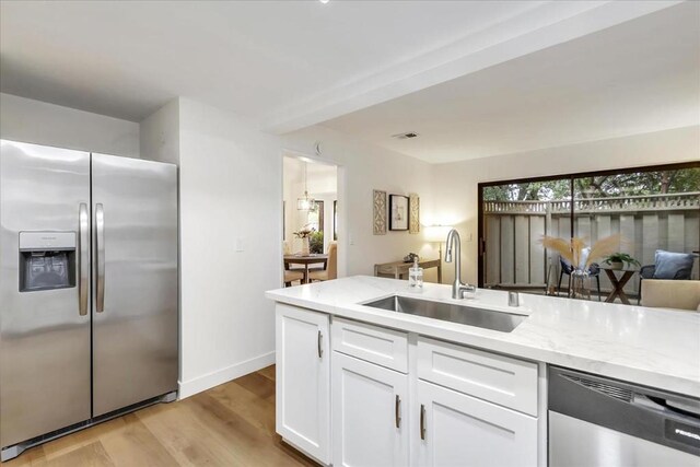 kitchen featuring sink, white cabinetry, stainless steel appliances, light stone counters, and light hardwood / wood-style floors