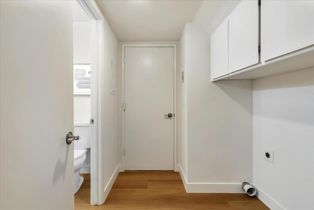 laundry area with electric dryer hookup, light hardwood / wood-style floors, and cabinets