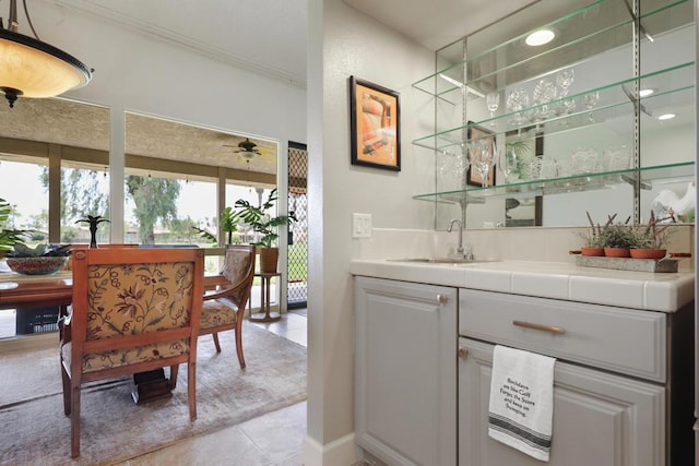 bar featuring light tile patterned flooring, tile countertops, sink, white cabinets, and ceiling fan