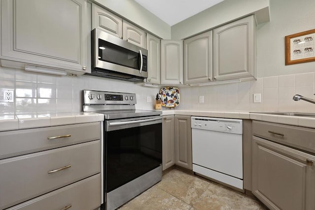 kitchen featuring backsplash, tile counters, gray cabinets, and appliances with stainless steel finishes