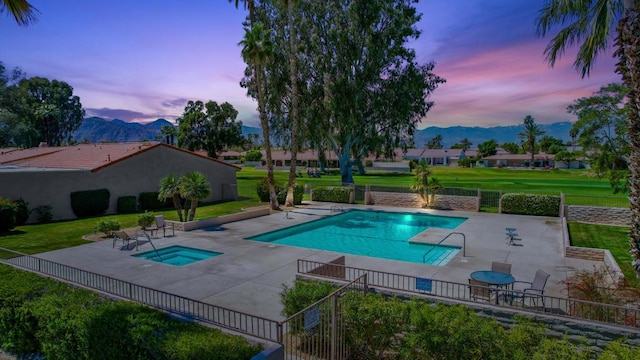 pool at dusk with a mountain view, a lawn, a hot tub, and a patio