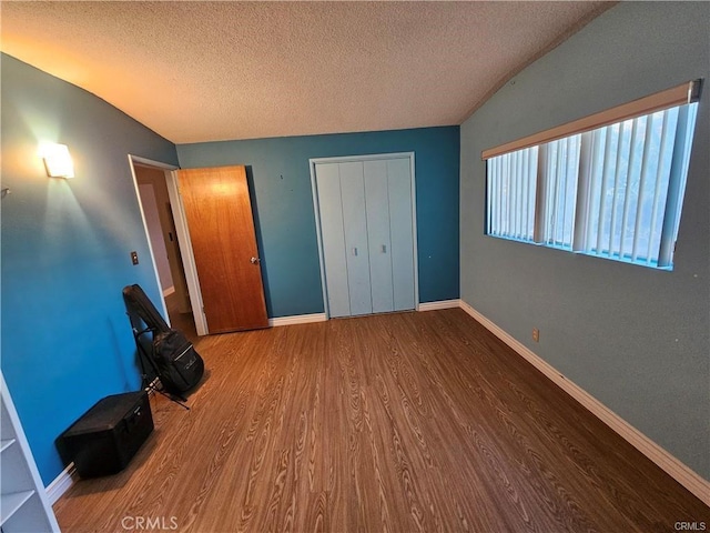 unfurnished bedroom featuring wood-type flooring, vaulted ceiling, a textured ceiling, and a closet