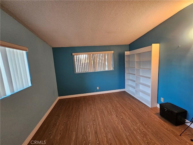 empty room with hardwood / wood-style flooring, lofted ceiling, and a textured ceiling