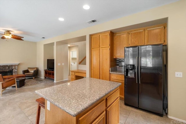 kitchen featuring visible vents, open floor plan, a center island, fridge with ice dispenser, and a brick fireplace