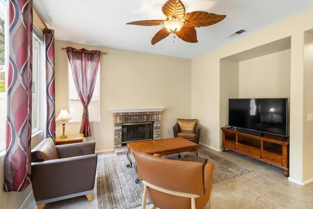 living room with a ceiling fan, a brick fireplace, visible vents, and baseboards