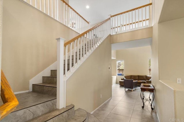 stairway featuring a towering ceiling, baseboards, and tile patterned floors