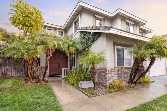 view of front of property with a garage, brick siding, fence, stucco siding, and a front yard