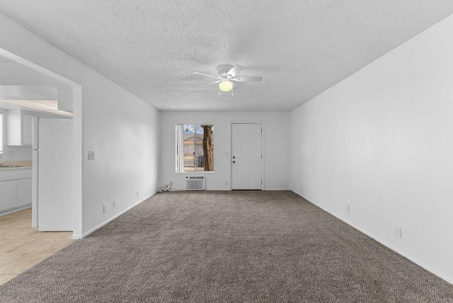 empty room with ceiling fan, light colored carpet, a wall unit AC, and a textured ceiling