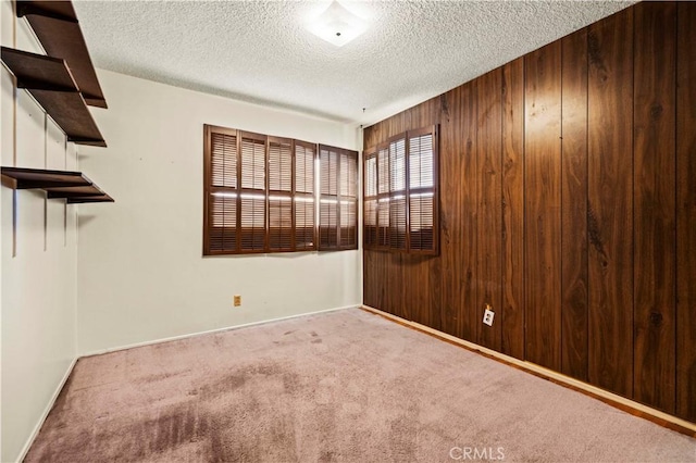 unfurnished room with light colored carpet, wooden walls, and a textured ceiling