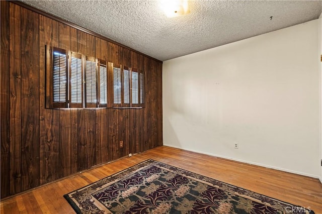 spare room featuring wood-type flooring, a textured ceiling, and wood walls