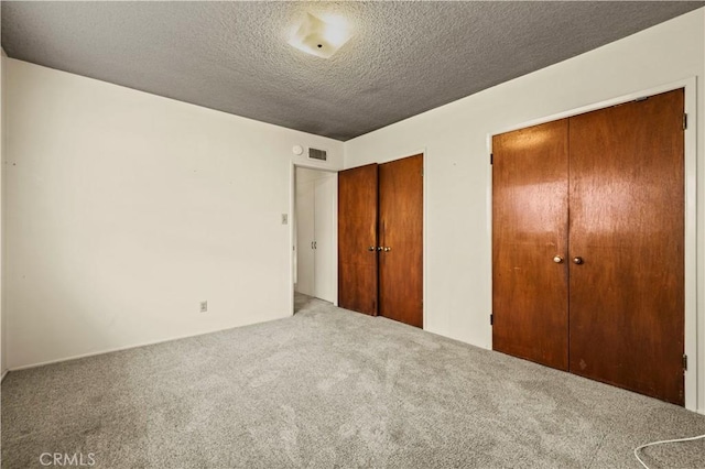 unfurnished bedroom with a textured ceiling, carpet, and two closets