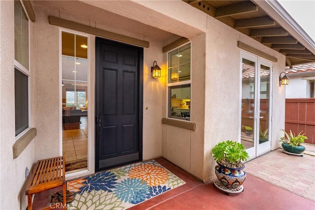 view of exterior entry featuring stucco siding, fence, a patio, and french doors