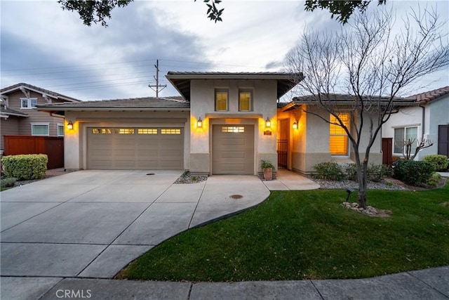 prairie-style home with a garage, concrete driveway, fence, a front lawn, and stucco siding