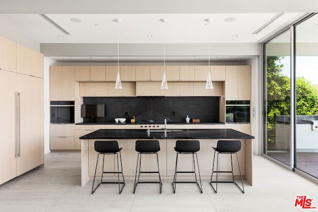 kitchen featuring sink, a kitchen island with sink, hanging light fixtures, decorative backsplash, and oven