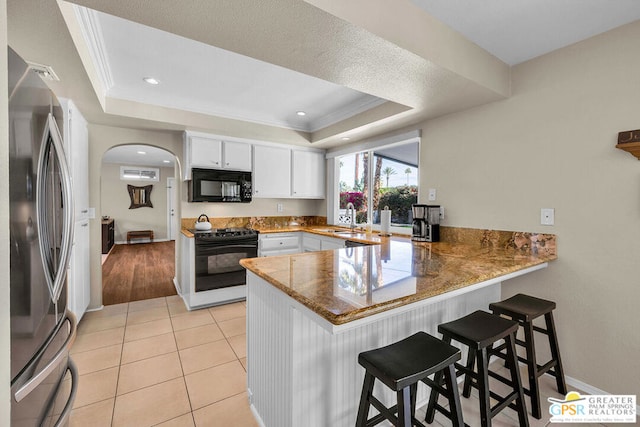 kitchen with stainless steel refrigerator, white cabinets, range, kitchen peninsula, and a raised ceiling